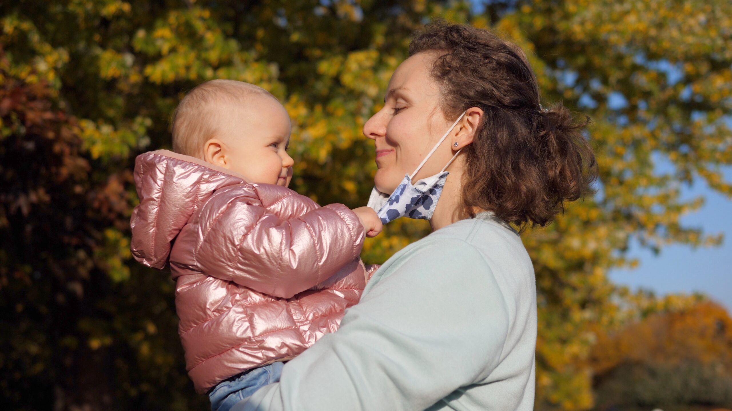 Autumn walks during covid 19 pandemic. Cute caucasian baby girl rips off a face mask of her moms and throws it away Illustrative photo